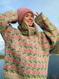 Woman in a taupe and pink floral knit turtleneck sweater with a pink beanie outdoors