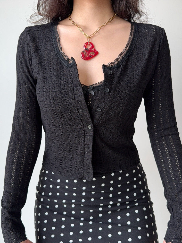 Close-up of a black cropped knit cardigan with a scoop neckline and lace details.