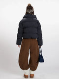 Back view of a woman in a cropped plaid puffer jacket, brown wide-leg pants, and a knit beanie with ear flaps.