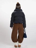 Back view of a woman in a cropped plaid puffer jacket, brown wide-leg pants, and a knit beanie with ear flaps.