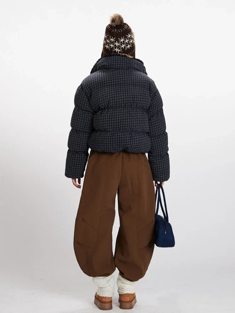 Back view of a woman in a cropped plaid puffer jacket, brown wide-leg pants, and a knit beanie with ear flaps.