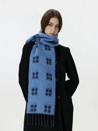 Woman wearing a blue scarf with a black windowpane plaid pattern and fringed hem