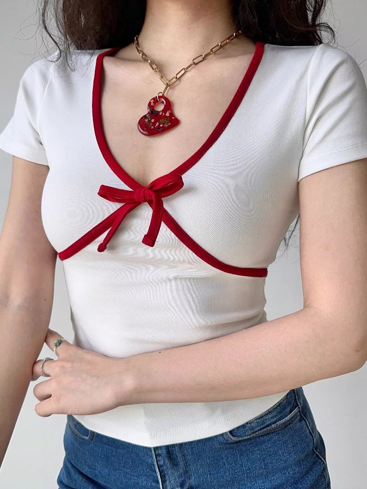 Woman wearing a white short-sleeve top with red trim and a bow accent