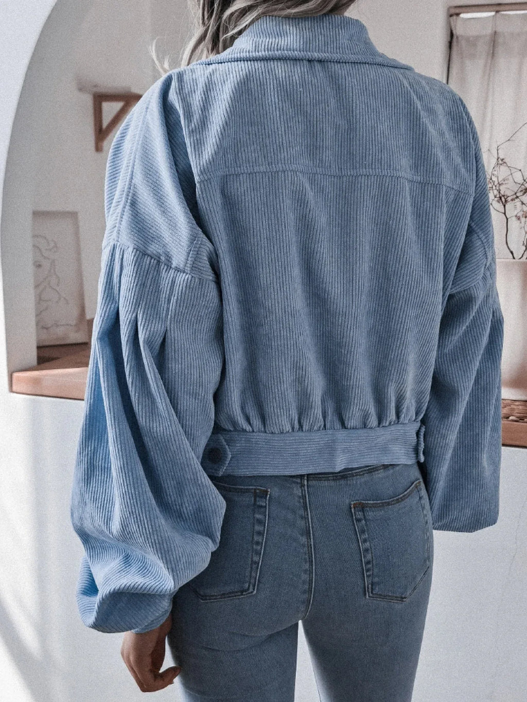 Back view of a woman in a light blue corduroy jacket, highlighting the balloon sleeves and cropped fit.