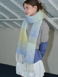 Side profile of a woman wearing a long, ombre gradient scarf in yellow, blue, and green, with fringed ends.