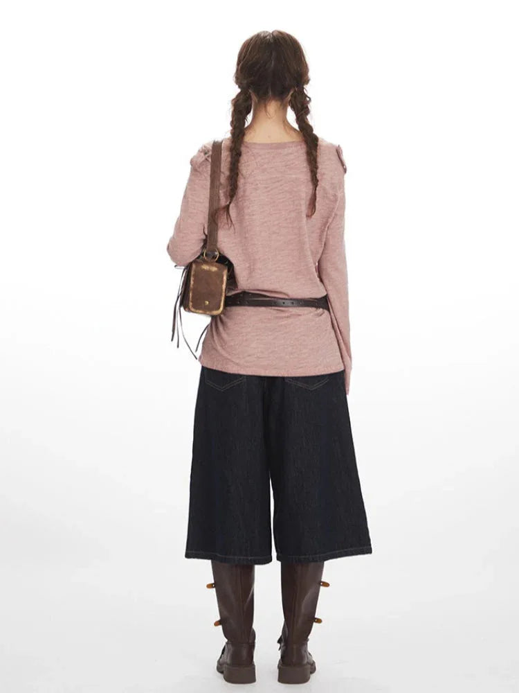 Back view of a woman wearing a dusty rose long-sleeve knit top with a V-neck and chest pocket, paired with dark wash wide-leg cropped jeans and brown boots. She has braids.