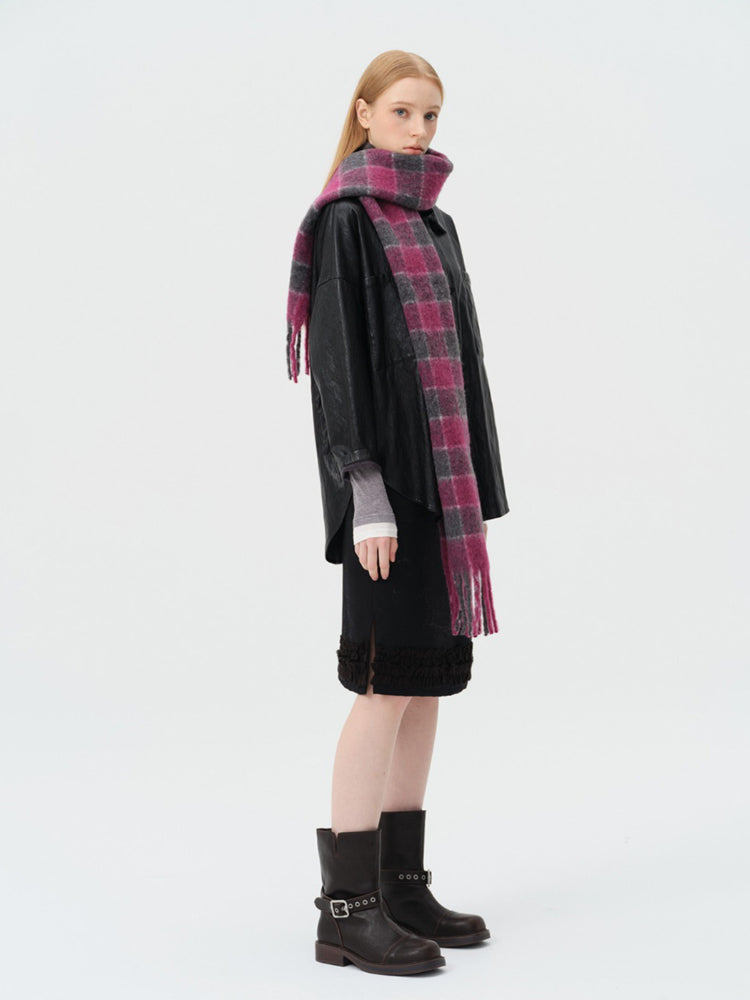 Three-quarter profile view of a woman wearing a black leather jacket, black skirt, and a pink and grey plaid scarf.
