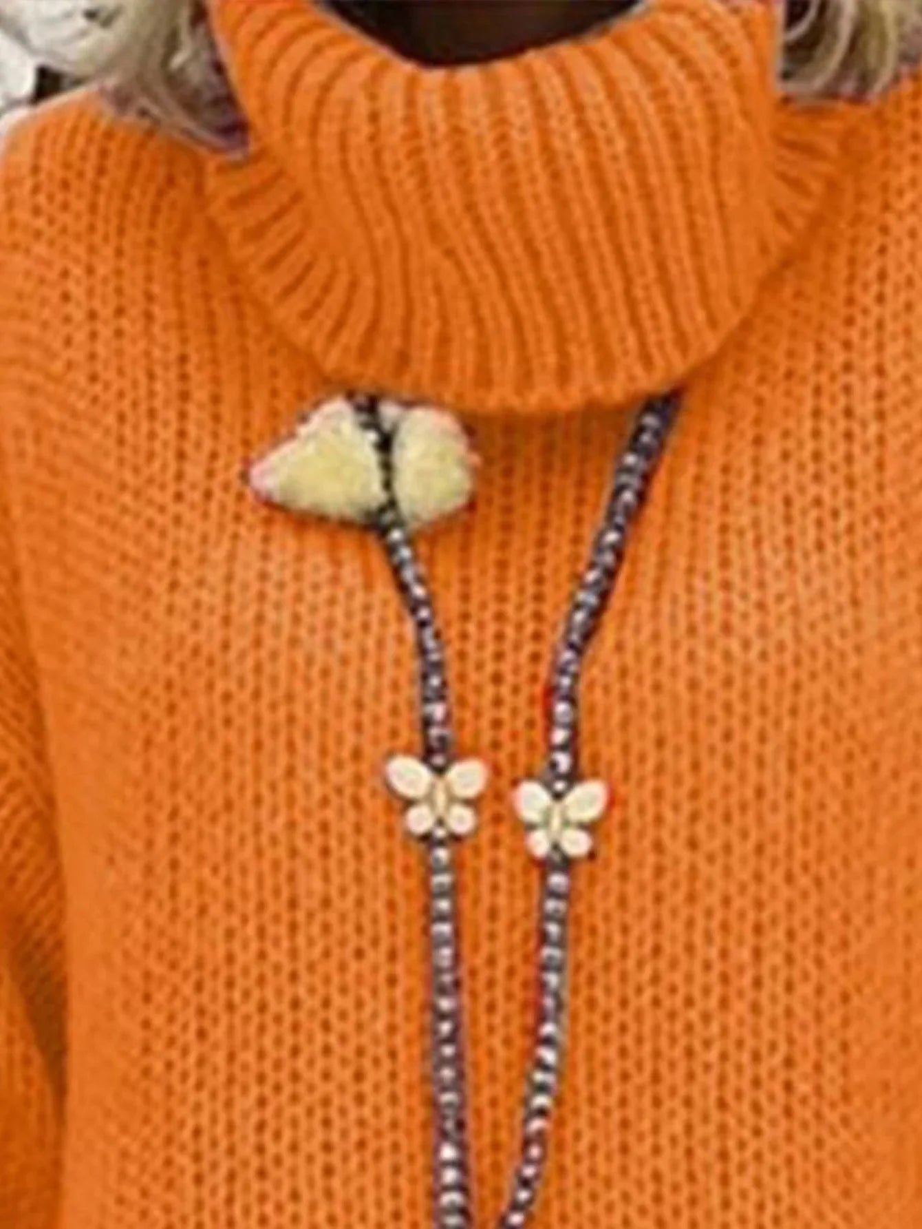 Close-up of the orange chunky knit turtleneck sweater showing the texture and the beaded necklace.