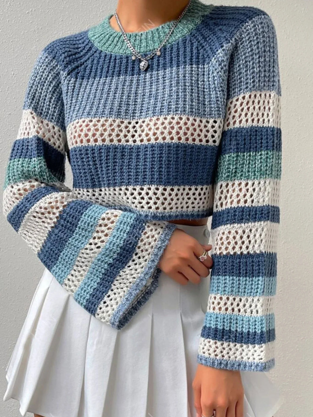 Front view detail of the bell sleeves on a blue, white, and green striped crochet knit cropped sweater.