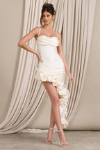 Side profile of a woman showcasing the fitted silhouette and ruffled hem of a cream satin dress.