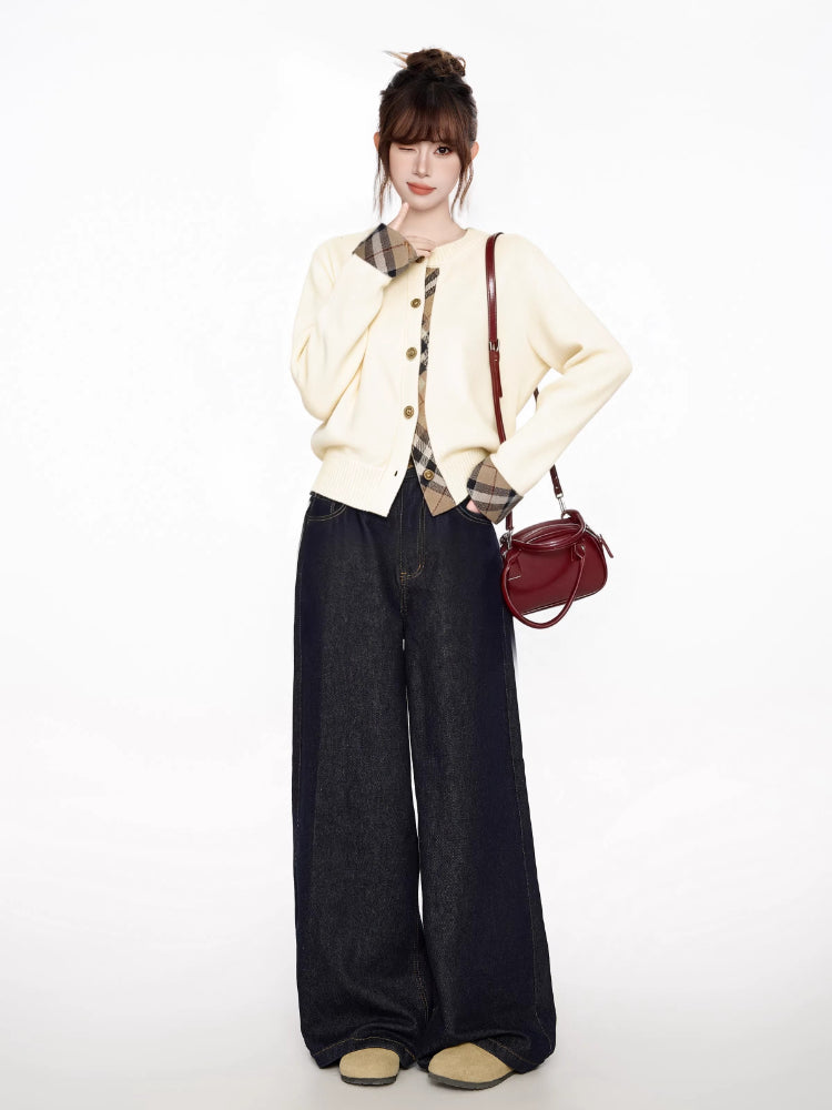 Woman posing in a cream cardigan with plaid trim, dark wide-leg jeans, and a red bucket bag.