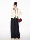 Woman posing in a cream cardigan with plaid trim, dark wide-leg jeans, and a red bucket bag.