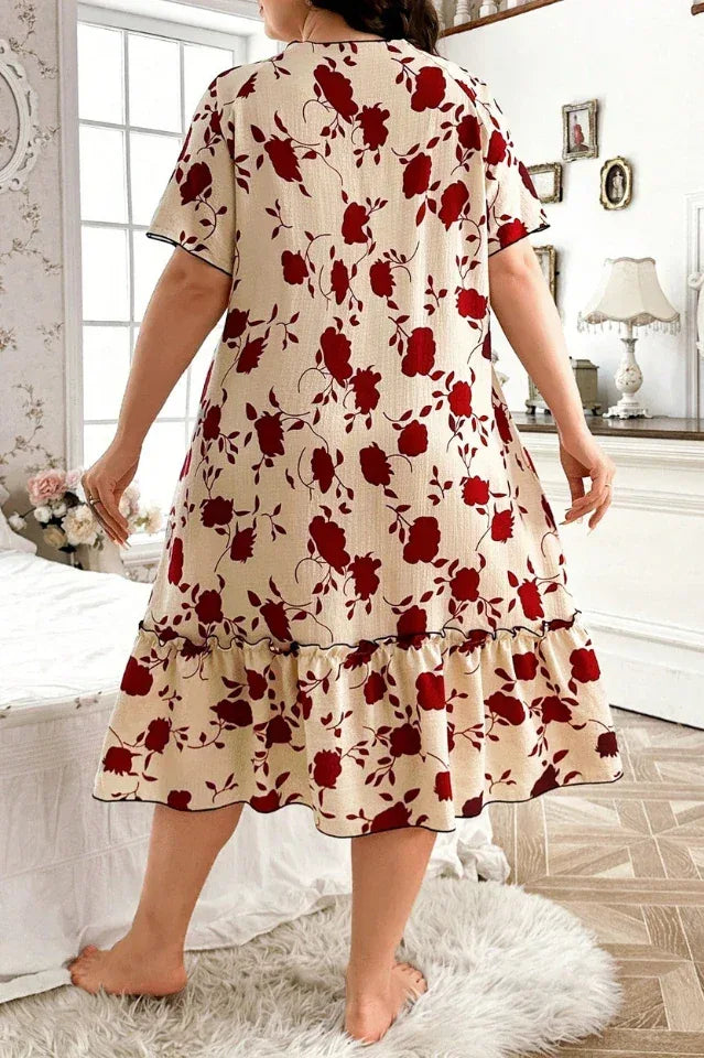 Plus-size woman wearing a cream-colored short-sleeve nightgown with a red floral print and ruffled hem, standing and showing the back view.