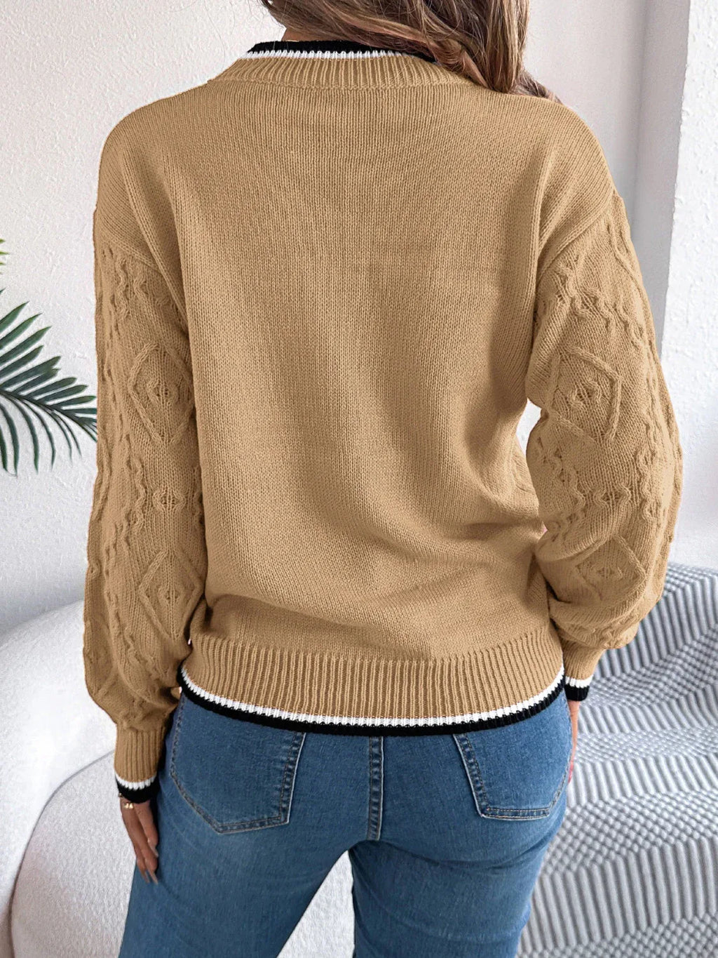 Back view of a woman wearing a tan sweater with a textured geometric pattern and striped trim.