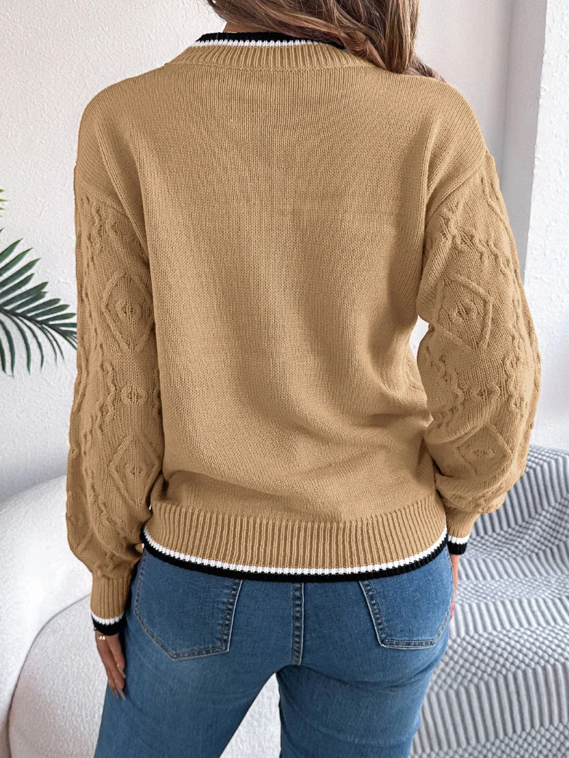 Back view of a woman wearing a tan sweater with a textured geometric pattern and striped trim.