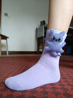 Close-up of a lavender ankle sock with a blue knitted teddy bear appliqué on the cuff.