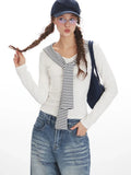 Woman in a white long-sleeve top with a striped collar and blue wide-leg jeans, posing with her hand in her pocket.