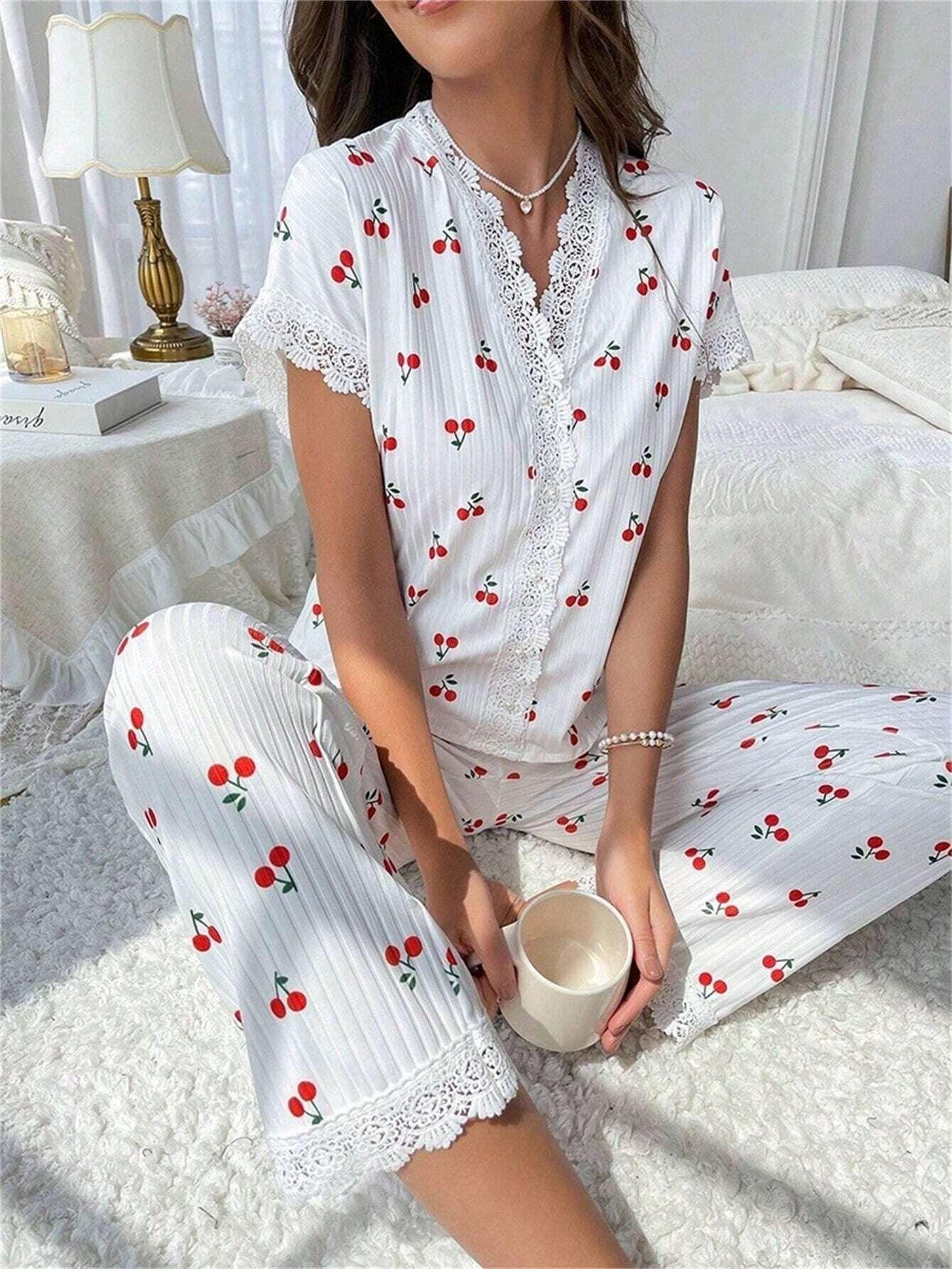 Woman sitting on a bed wearing a white cherry print pajama set with lace detailing and holding a mug.