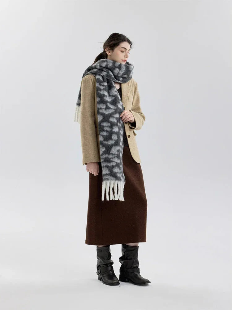 Full body shot of a woman in a beige blazer, brown skirt, and a grey and white leopard print fuzzy scarf with fringe trim.