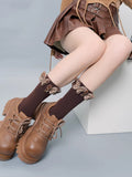 Brown ribbed crew socks with decorative butterfly embellishments at the cuff, paired with brown platform lace-up shoes and a brown pleated skirt.