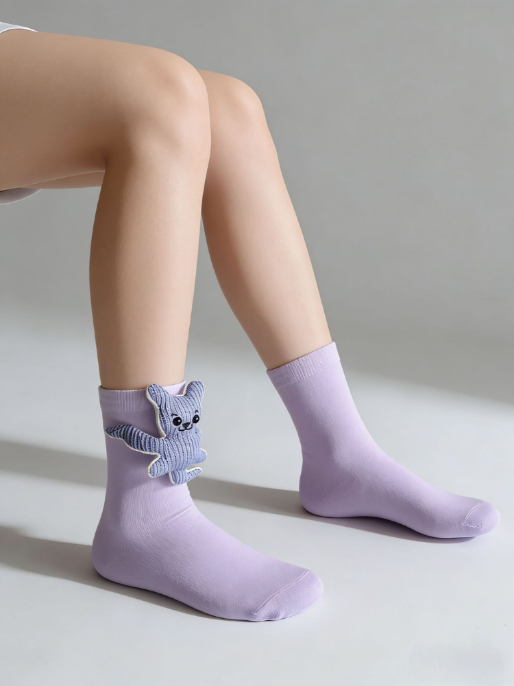 A person wearing lavender ankle socks with a blue knitted teddy bear appliqué on one sock.