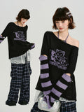 Woman modeling a black knit sweater with purple and black striped sleeves and cutouts.