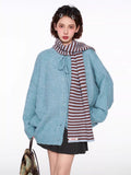Woman wearing a blue knit cardigan with a tie closure and button front, styled with a pleated skirt and striped scarf.