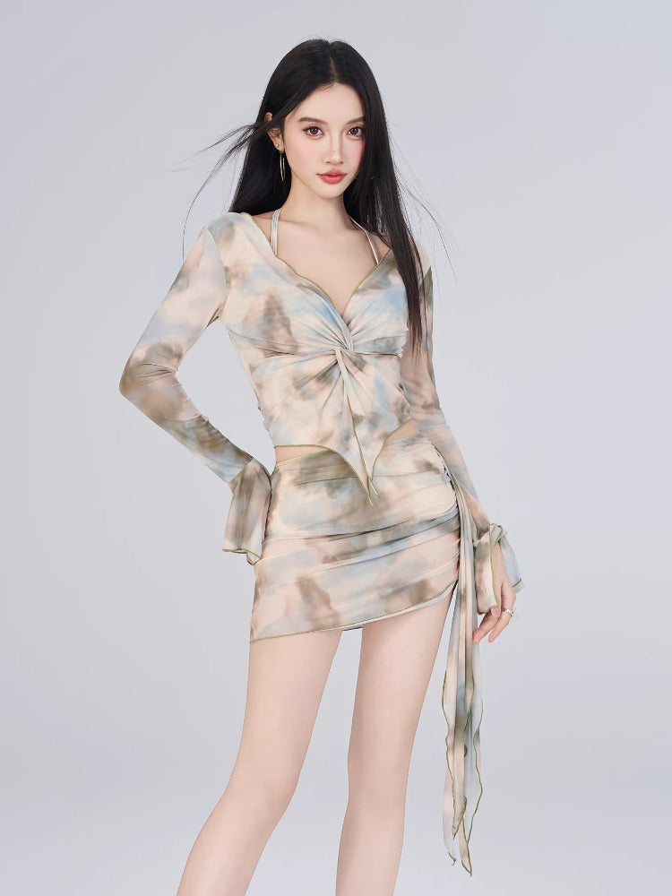 Full body shot of a woman in a sheer abstract print two-piece set with a tie-front top and ruched skirt.