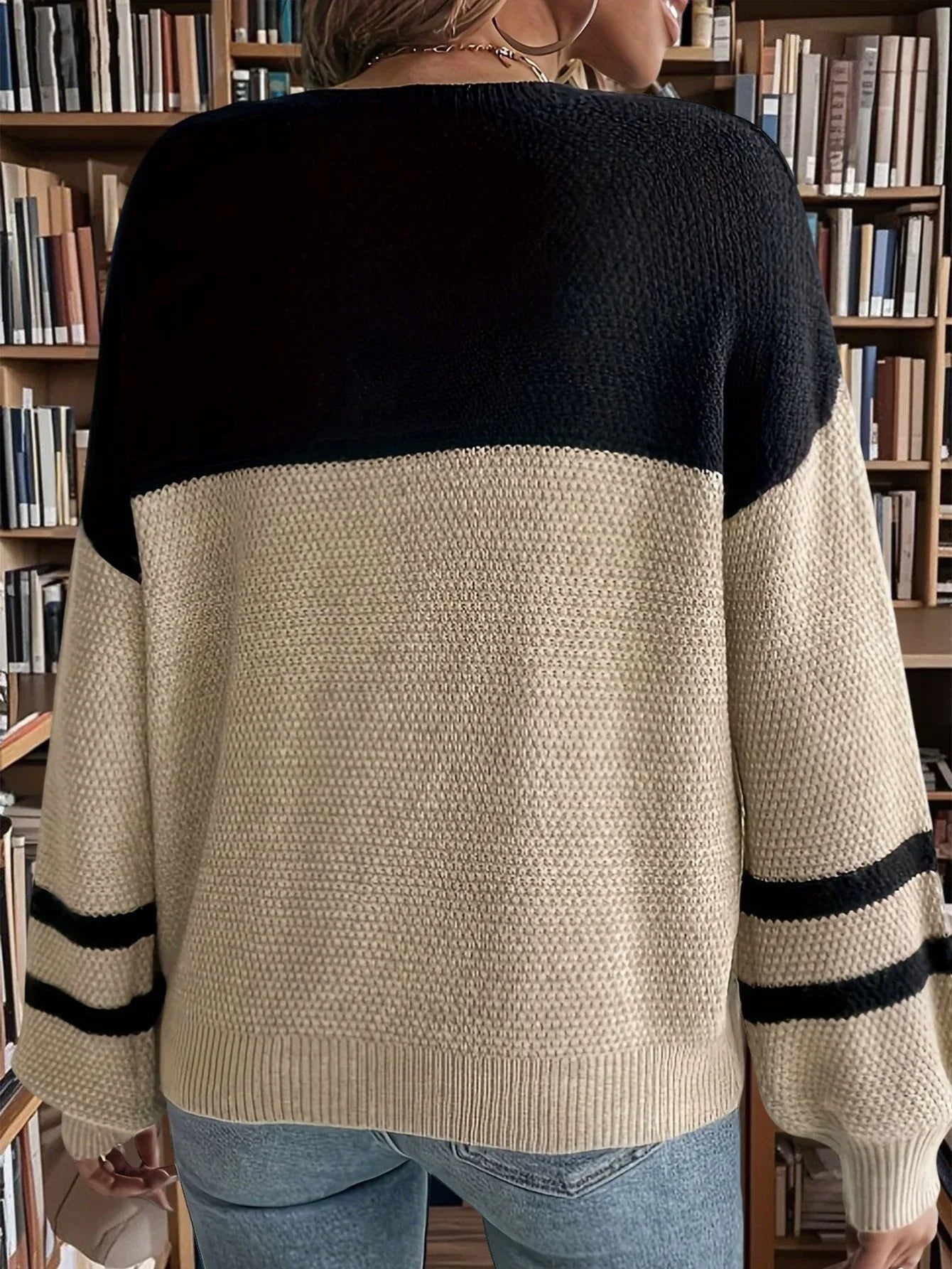 Back view of a woman wearing a black and beige color block knit sweater with striped sleeves.