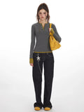 Woman wearing a grey long-sleeve Henley top with contrast green cuffs and hem, dark wash baggy jeans, and a yellow handbag