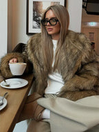 Woman with blonde hair wearing a luxurious brown faux fur coat indoors.