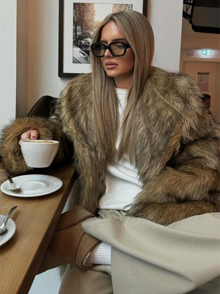 Woman with blonde hair wearing a luxurious brown faux fur coat indoors.