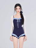 Woman wearing a navy blue one-piece swimsuit with light blue ruffled trim and a white sheer cardigan
