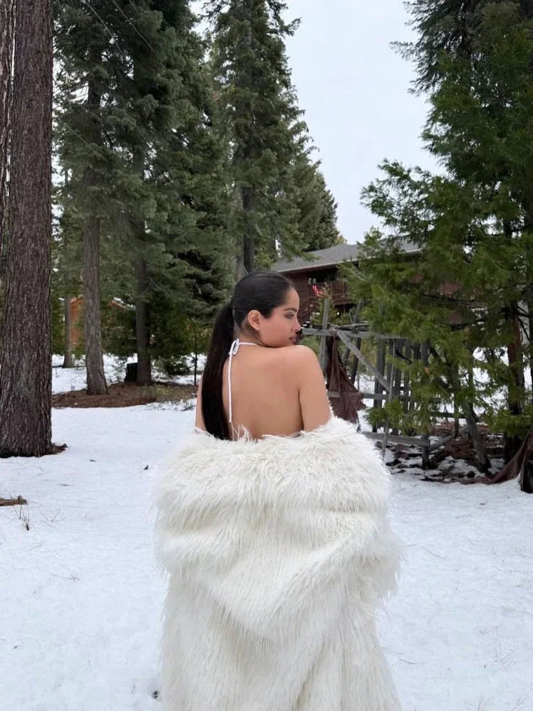 Back view of a woman wearing a white faux fur coat in a snowy forest