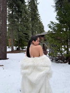 Back view of a woman wearing a white faux fur coat in a snowy forest