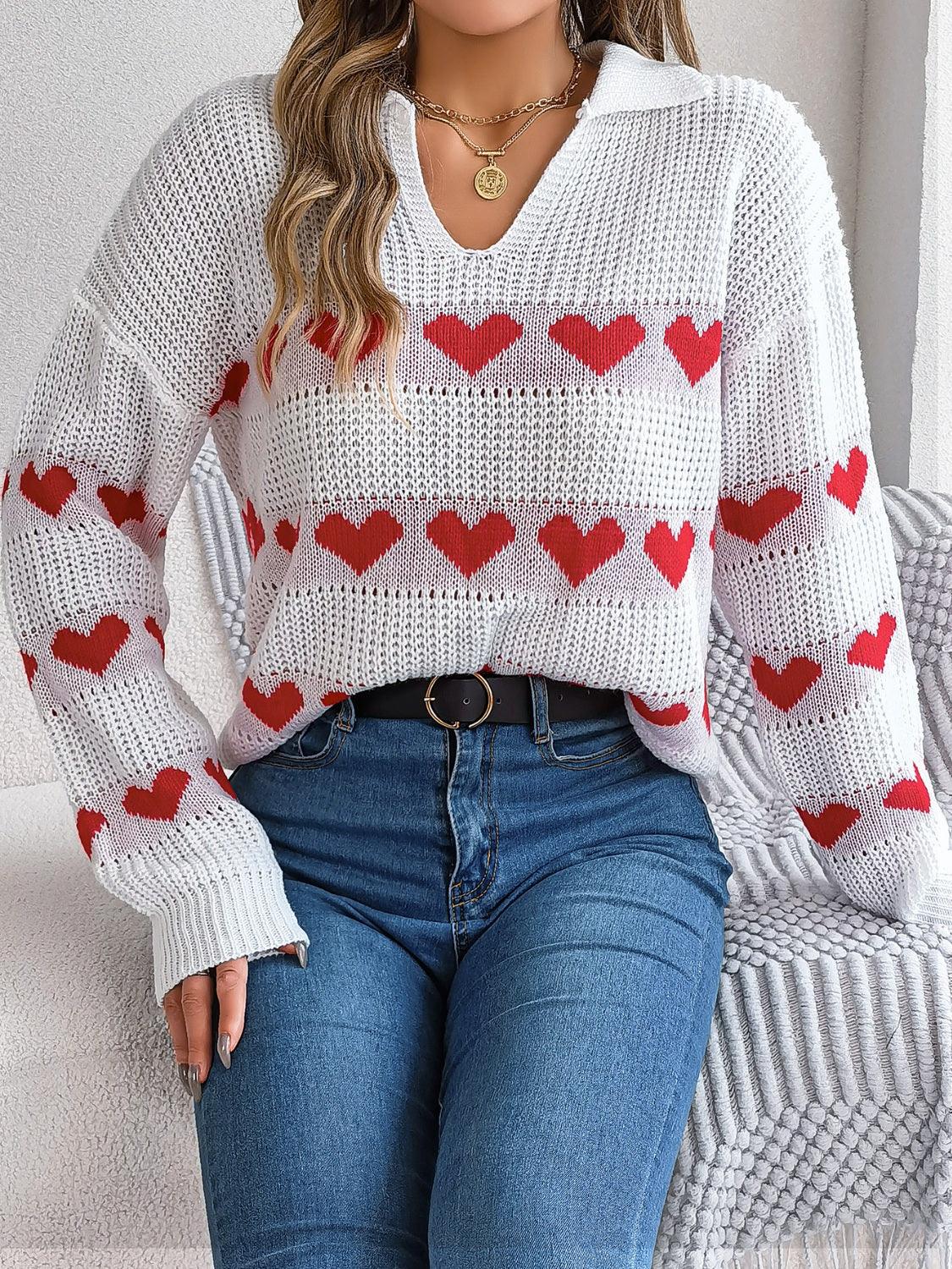 Woman in a white knit sweater with red hearts, blue jeans, and a belt.