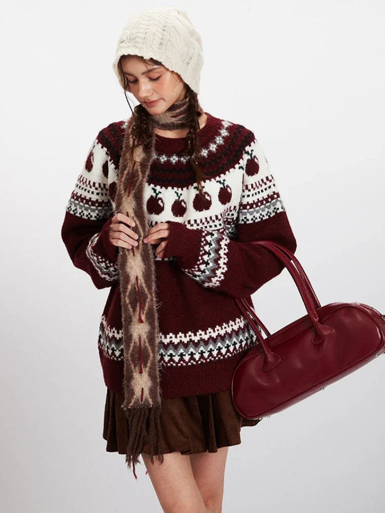 Close-up of a woman wearing a burgundy Fair Isle sweater with apple motif, a patterned scarf, and a white knit hat