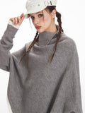 Woman wearing a grey knit poncho, adjusting her white hat.