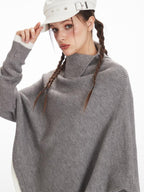 Woman wearing a grey knit poncho, adjusting her white hat.