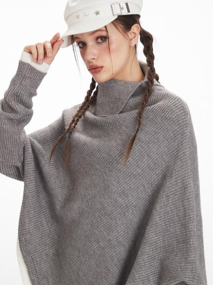 Woman wearing a grey knit poncho, adjusting her white hat.