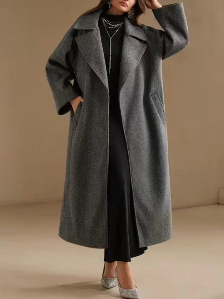 Full body shot of a woman in a long grey wool blend coat, styled with a black dress and sparkling heels.