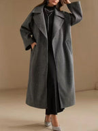 Full body shot of a woman in a long grey wool blend coat, styled with a black dress and sparkling heels.
