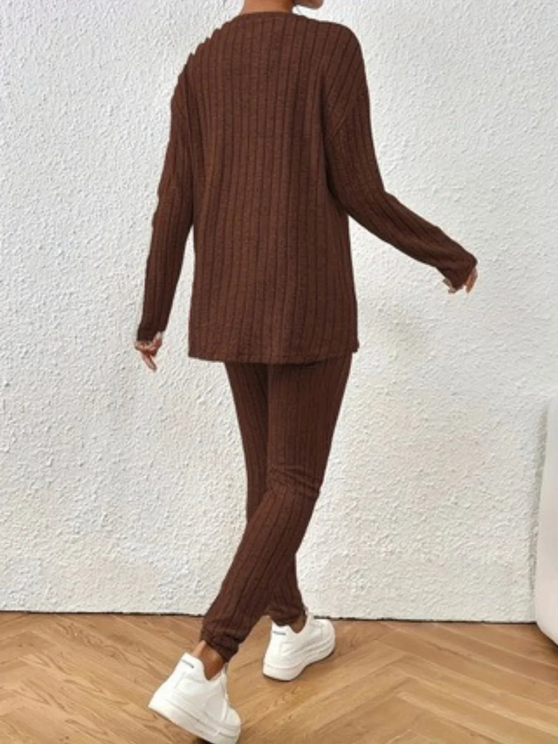 Woman wearing a brown ribbed knit loungewear set with a crew neck top and slim-fit pants, sitting on a white couch.