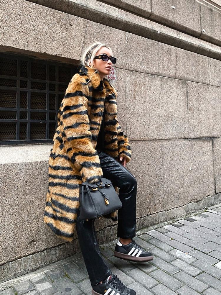 Woman in a faux fur tiger stripe coat, black pants, and sneakers.
