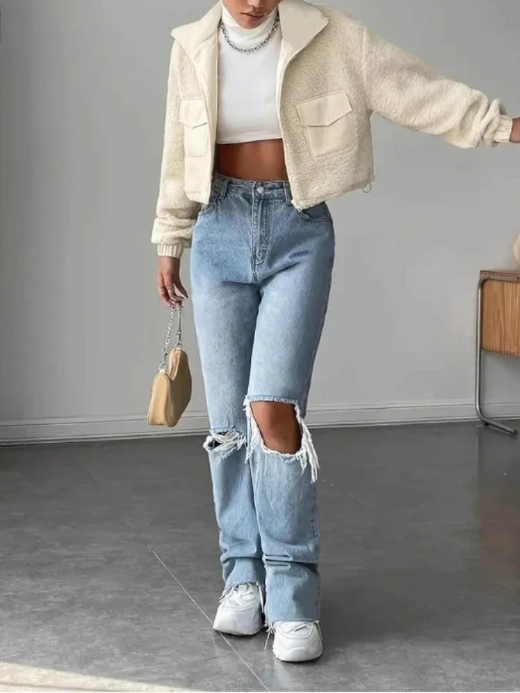 Woman in a cream sherpa fleece cropped jacket, white turtleneck, and ripped blue jeans.