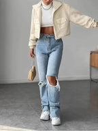 Woman in a cream sherpa fleece cropped jacket, white turtleneck, and ripped blue jeans.