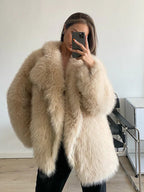 Woman wearing a brown shaggy faux fur coat and blue jeans sitting on a couch outdoors.