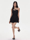 Full body shot of a woman in a black one-shoulder dress with a tiered skirt, posing with one leg raised
