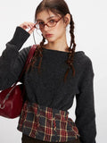 Detail shot of a model's face and upper body, showcasing the dark grey knit cropped sweater with plaid waistband accent.