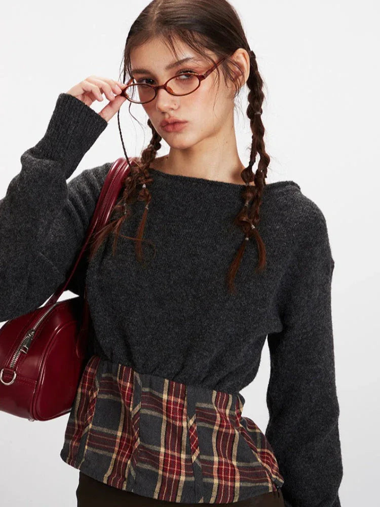Detail shot of a model's face and upper body, showcasing the dark grey knit cropped sweater with plaid waistband accent.